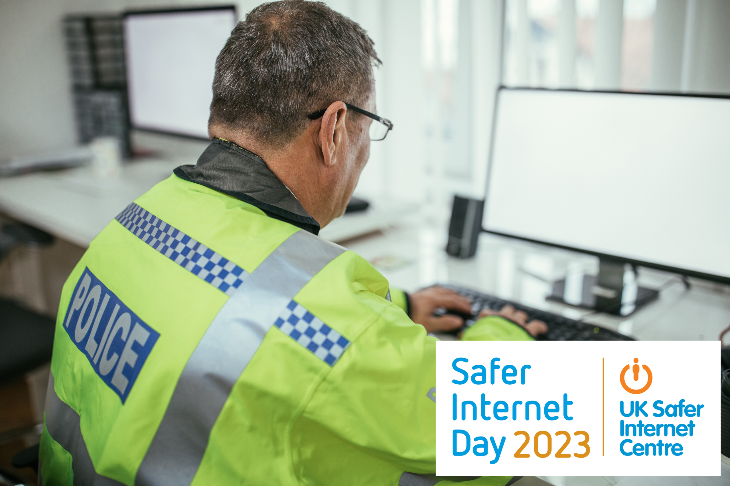 A male Police Officer uses a computer. In the corner of the image is the Safer Internet Day logo.