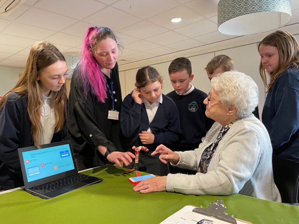 Digital Heroes from Cornist Park School show an elderly women how to do something on her mobile device.