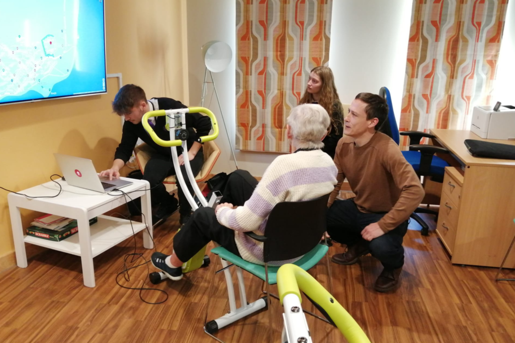 DCW Digital Advisors Deian ap Rhisiart and pupils from Ysgol David Hughes show a resident at Hafan Cegni how to use a digital bike.