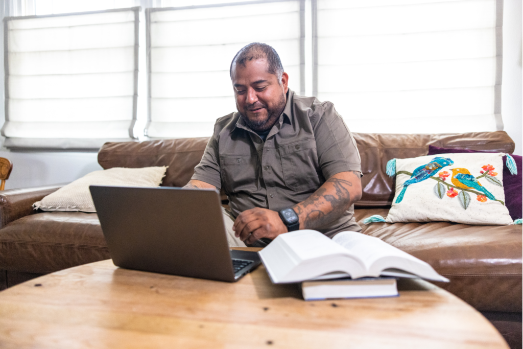 A man sits on a sofa while working on a laptop