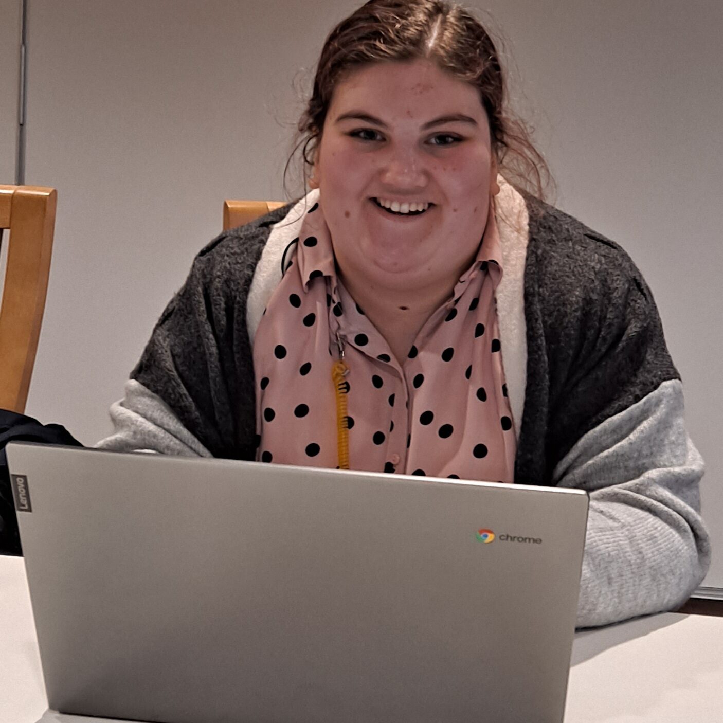 A photograph of Erin O'Donnell, Clywd Alyn's Community Assistant and DFN Search Intern. She smiles as she sits at a desk with a Chromebook in front of her.