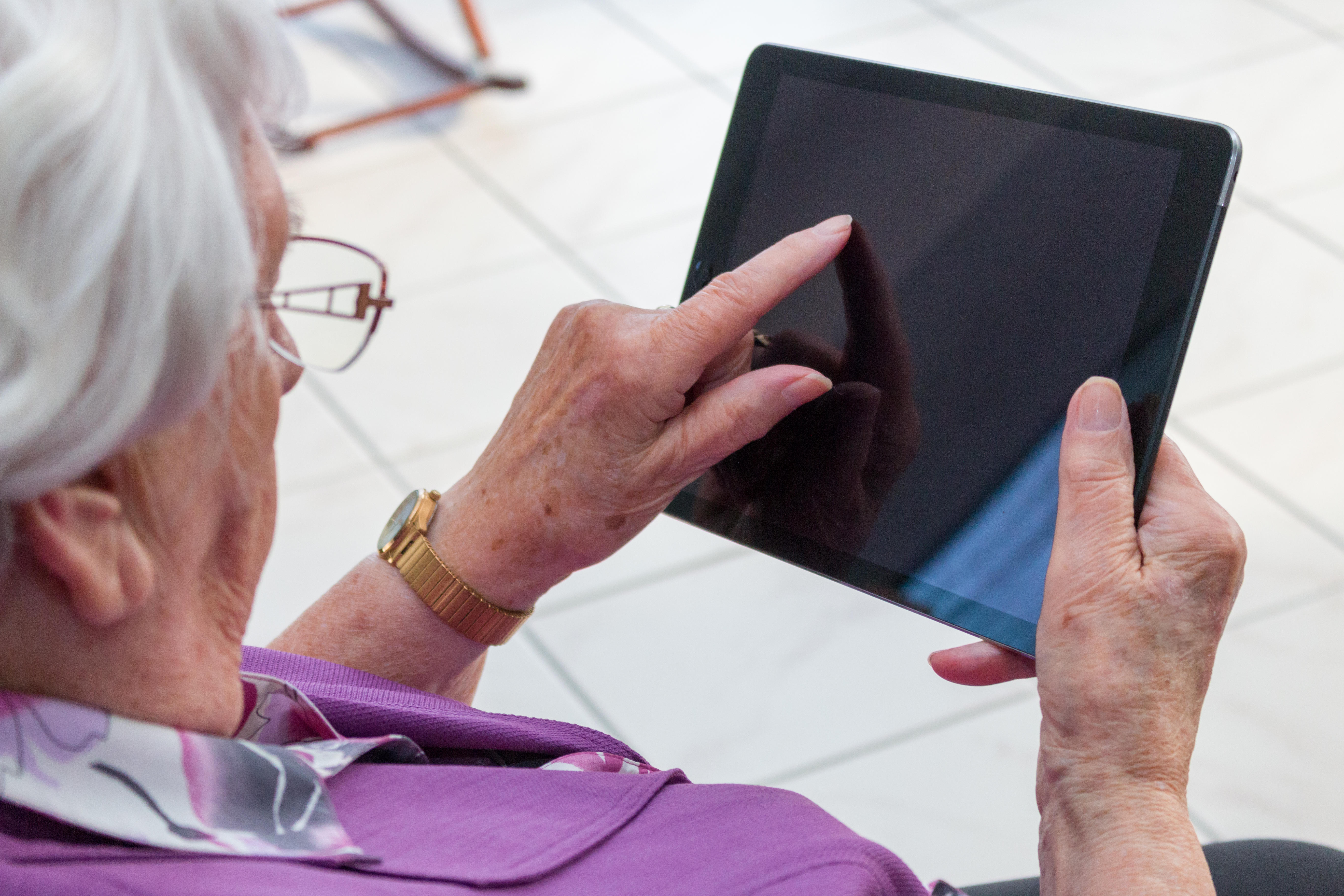 Menyw 95 oed yn eistedd yn yr ystafell fyw yn teipio ar ddyfais symudol neu iPad