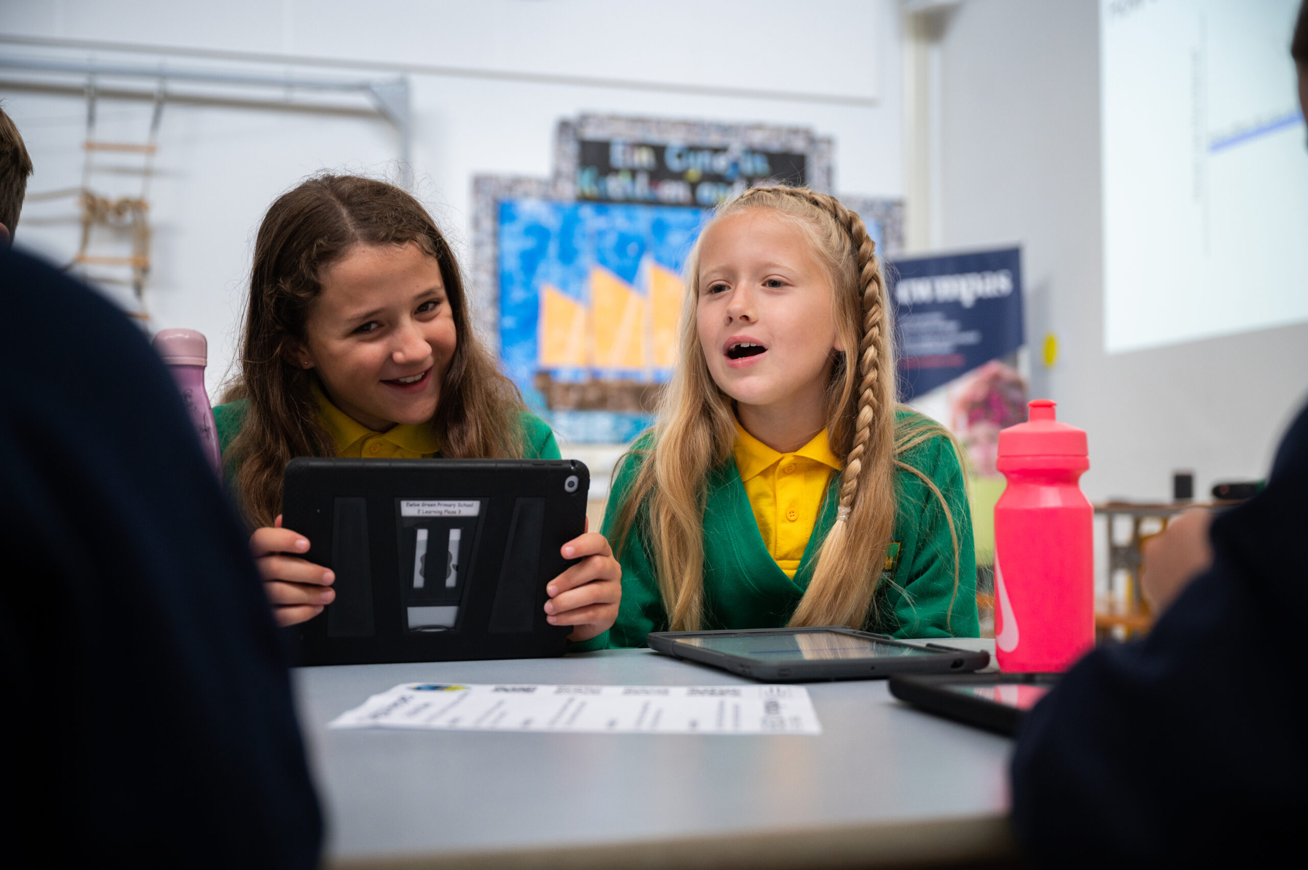 Ffotograff o ddwy ferch ysgol gynradd yn defnyddio dyfeisiau tabled. Mae'r ddau yn cymryd rhan mewn sesiwn Arwyr Digidol.