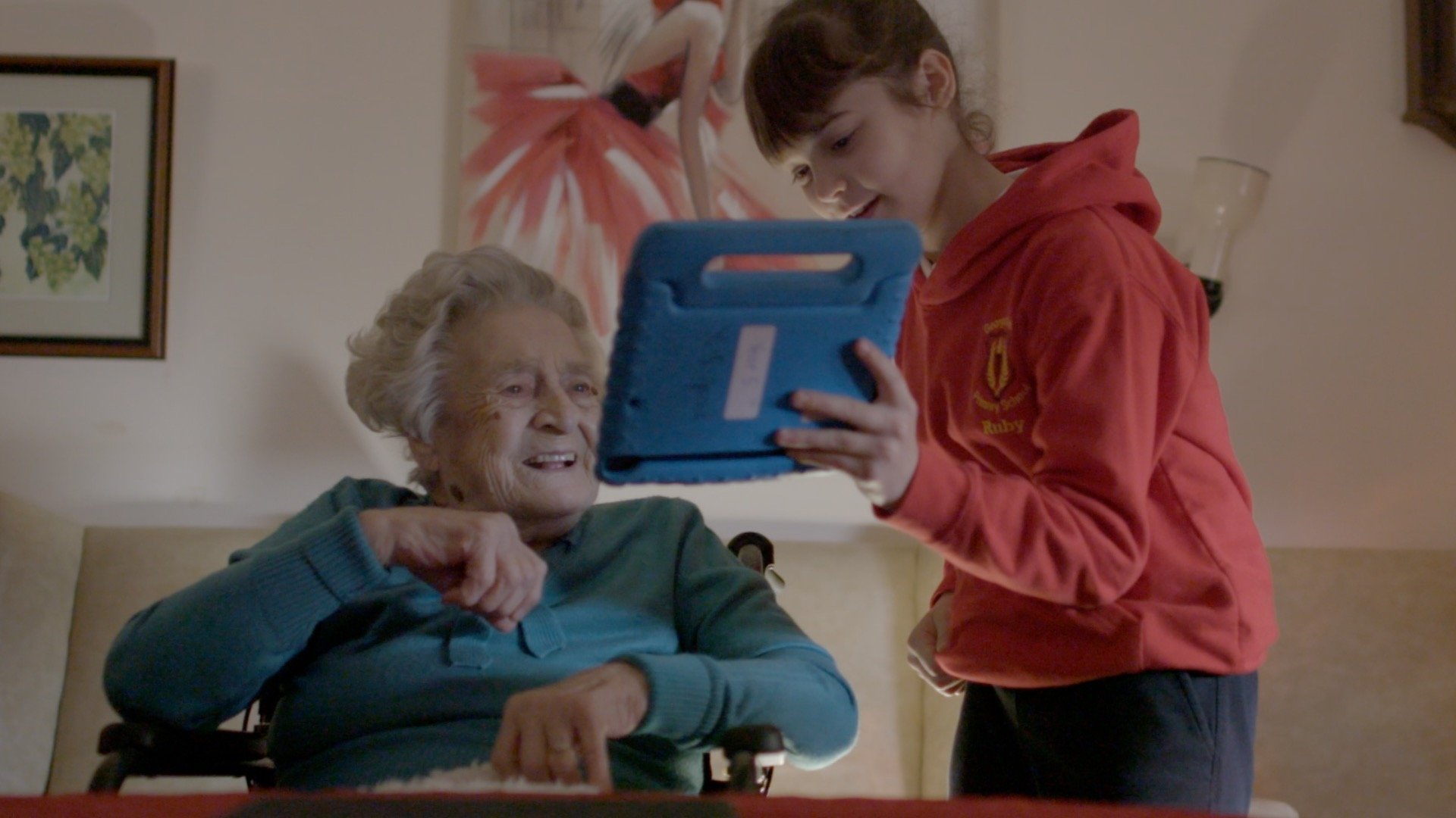 A photograph of a female school pupil Digital Hero standing next to a senior lady, showing her something on a tablet device.