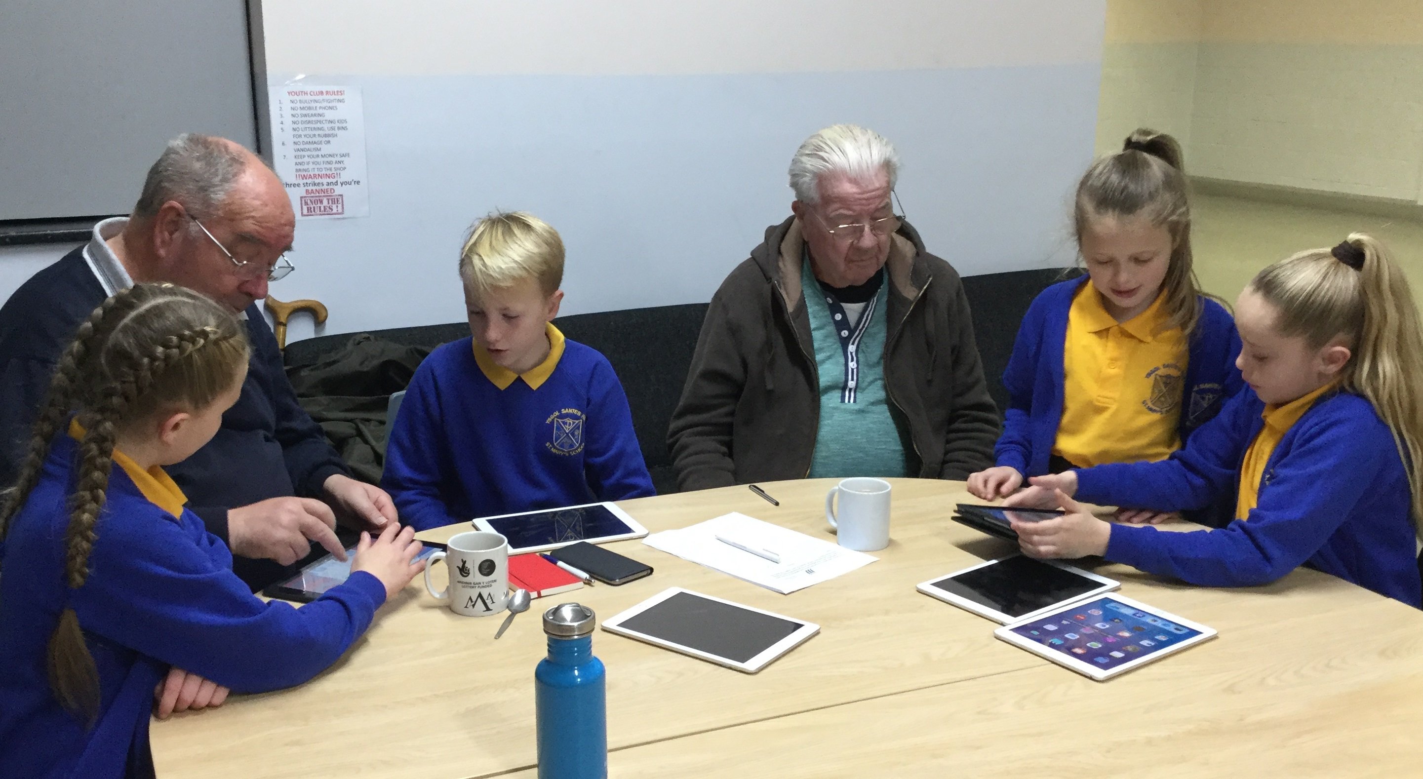 school children show two older men how to use a tablet device