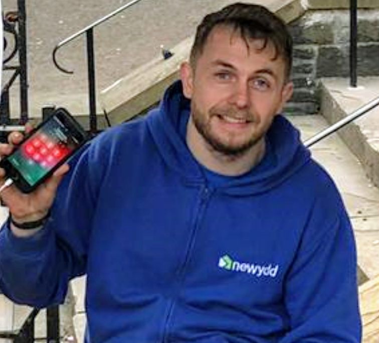 A picture of  Scott Tandy of Newydd Housing holding up a mobile phone