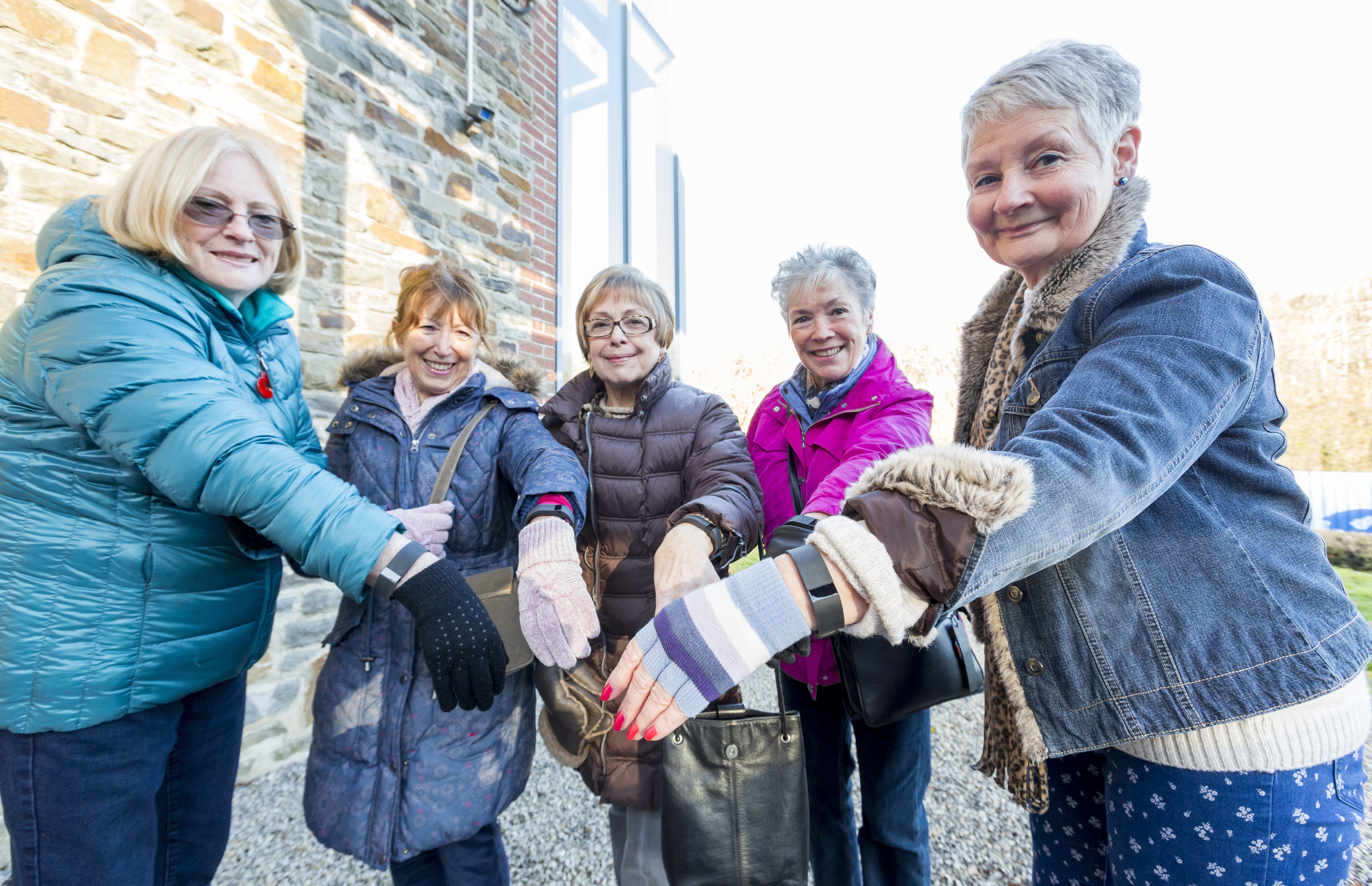 A group of five standing ladies holding their smart fitness wristbands to the camera