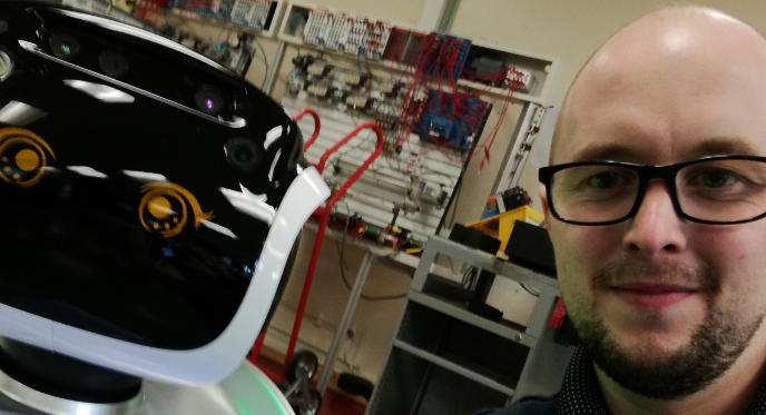 A selfie photograph of Ashley Bale of Innovate Trust next to a robot in a workshop.