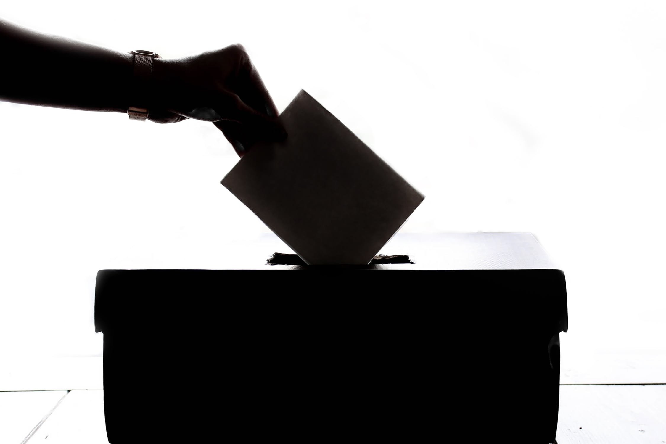 A silhouette photograph of a hand posting a note into a ballot box.