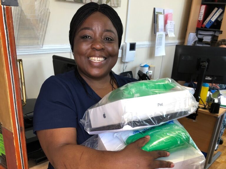 A smiling care home nurse holding equipment loaned by Digital Communities Wales.