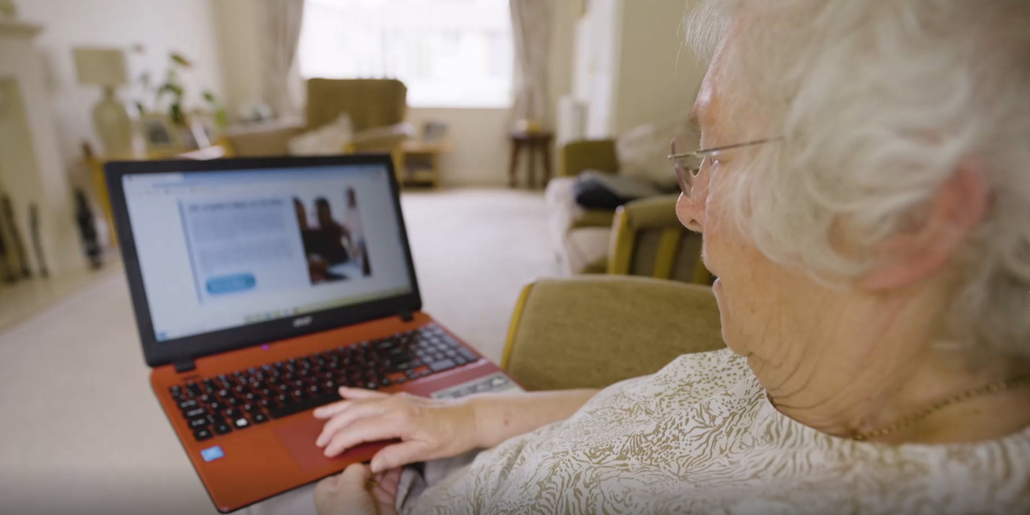 An over the shoulder photograph of a senior lady sat down looking at the Digital Communities Wales website on the laptop in front of her.