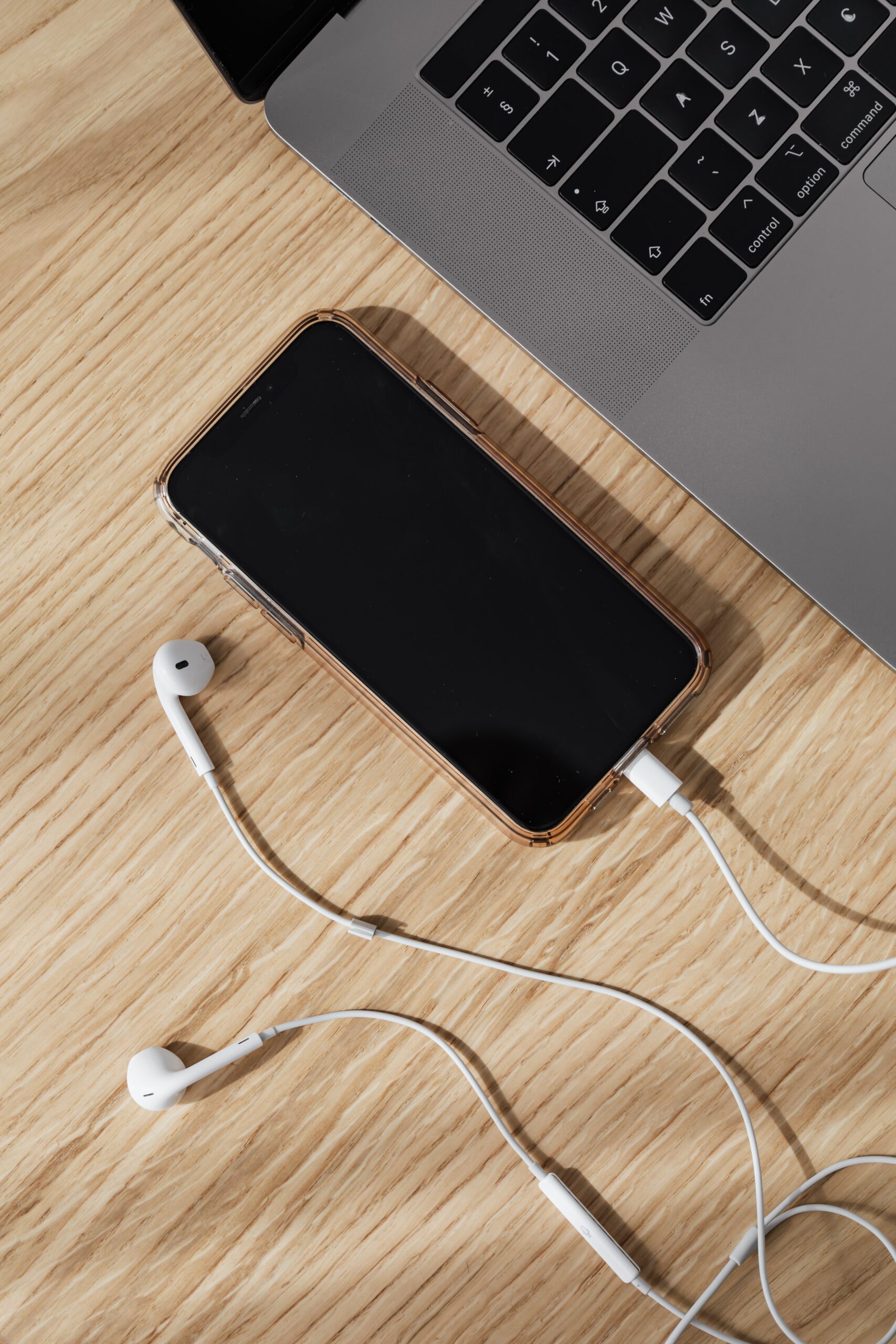 A photo of an iPhone with wired headphones and a laptop on a desk.
