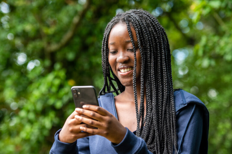A photograph of Melissa Denga, a college student, standing whilst smiling looking down at her smartphone.