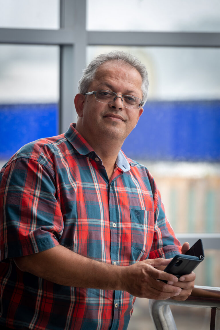 A photograph of Shahsawar Rahmani. He is stood up, looking at the camera whilst holding a smartphone.