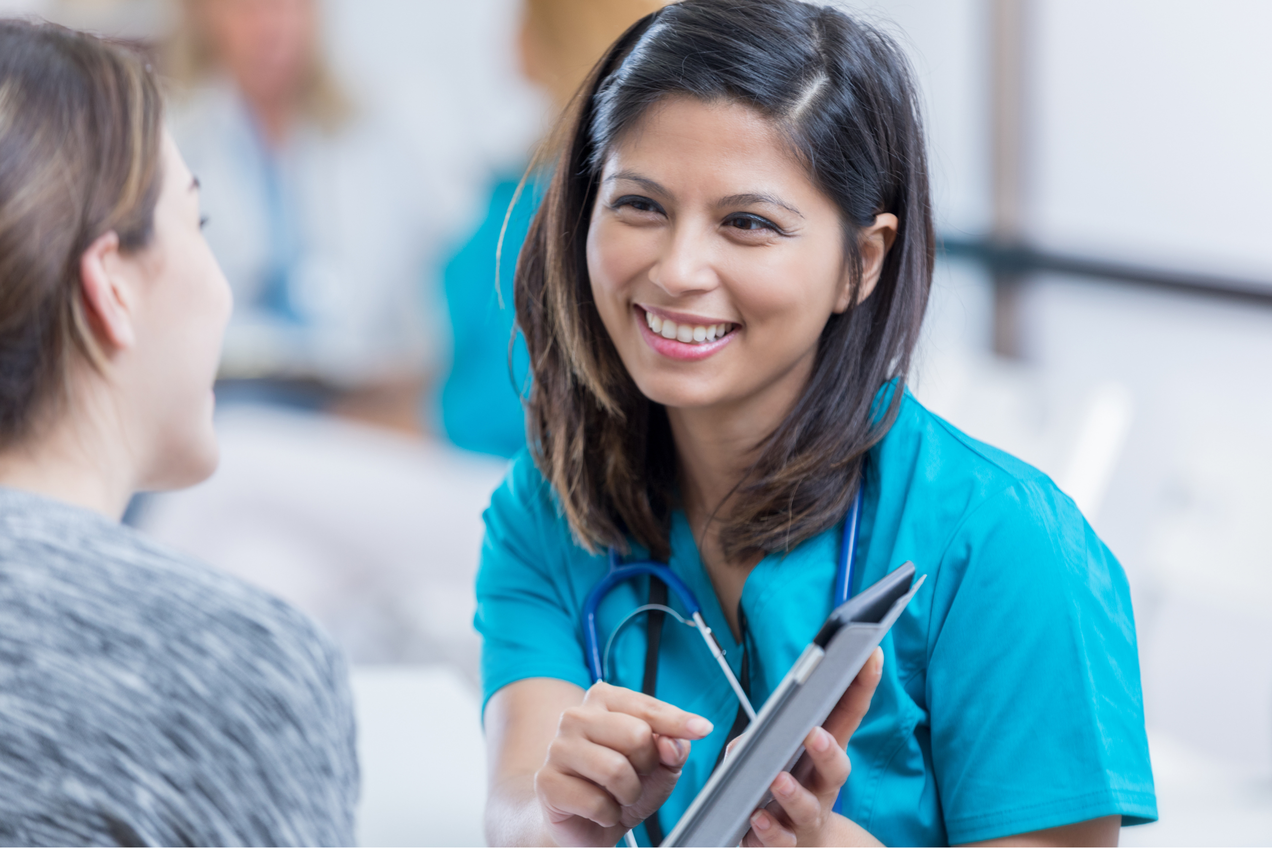 An image of a female medical professional holding and pointing at a tablet device while smiling and looking at a young female patient.