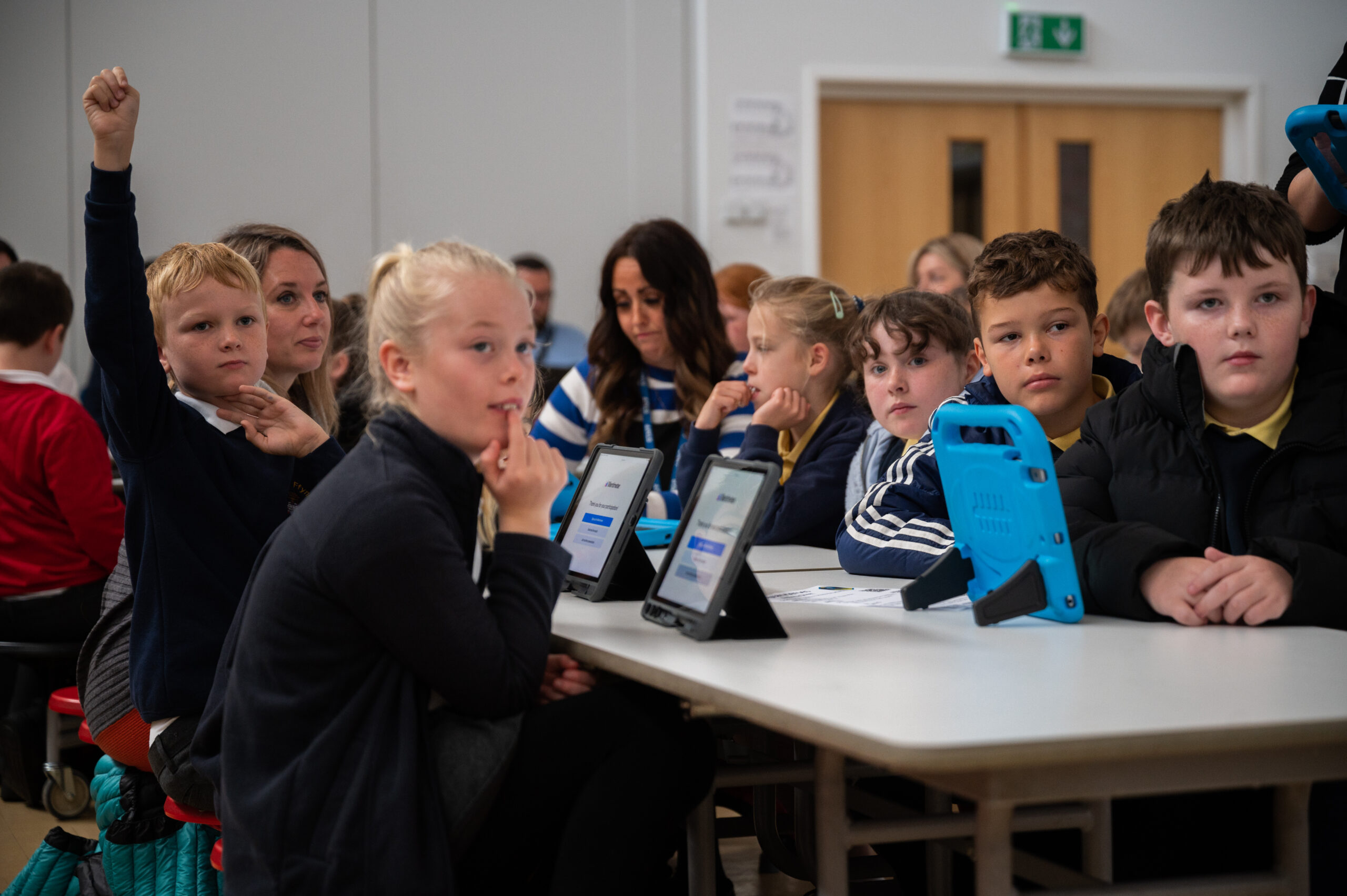 A photograph of six school children and two teachers sat around a desk participating in a Digital Heroes session.