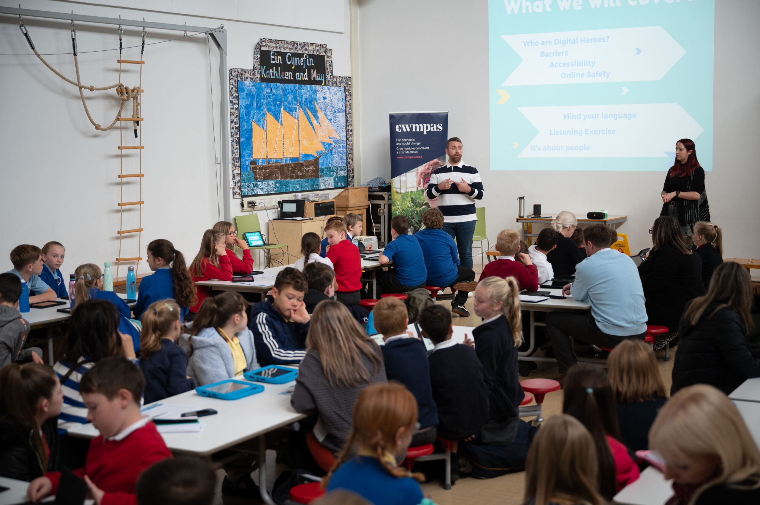 A photograph of two DCW staff members leading a Digital Heroes session in a classroom full of children.