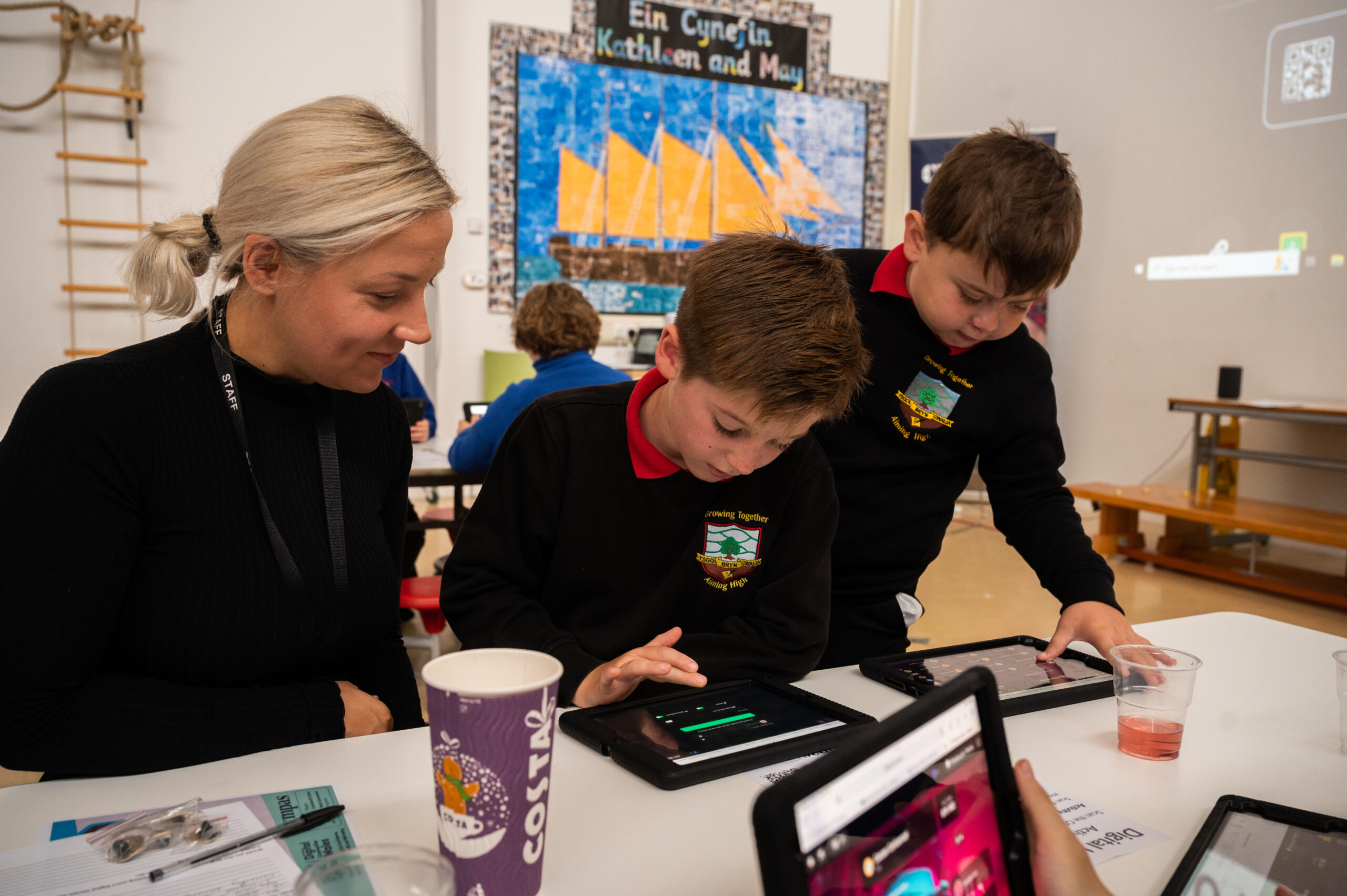 A photograph of two male primary school aged Digital Heroes and their teacher using two tablet devices.