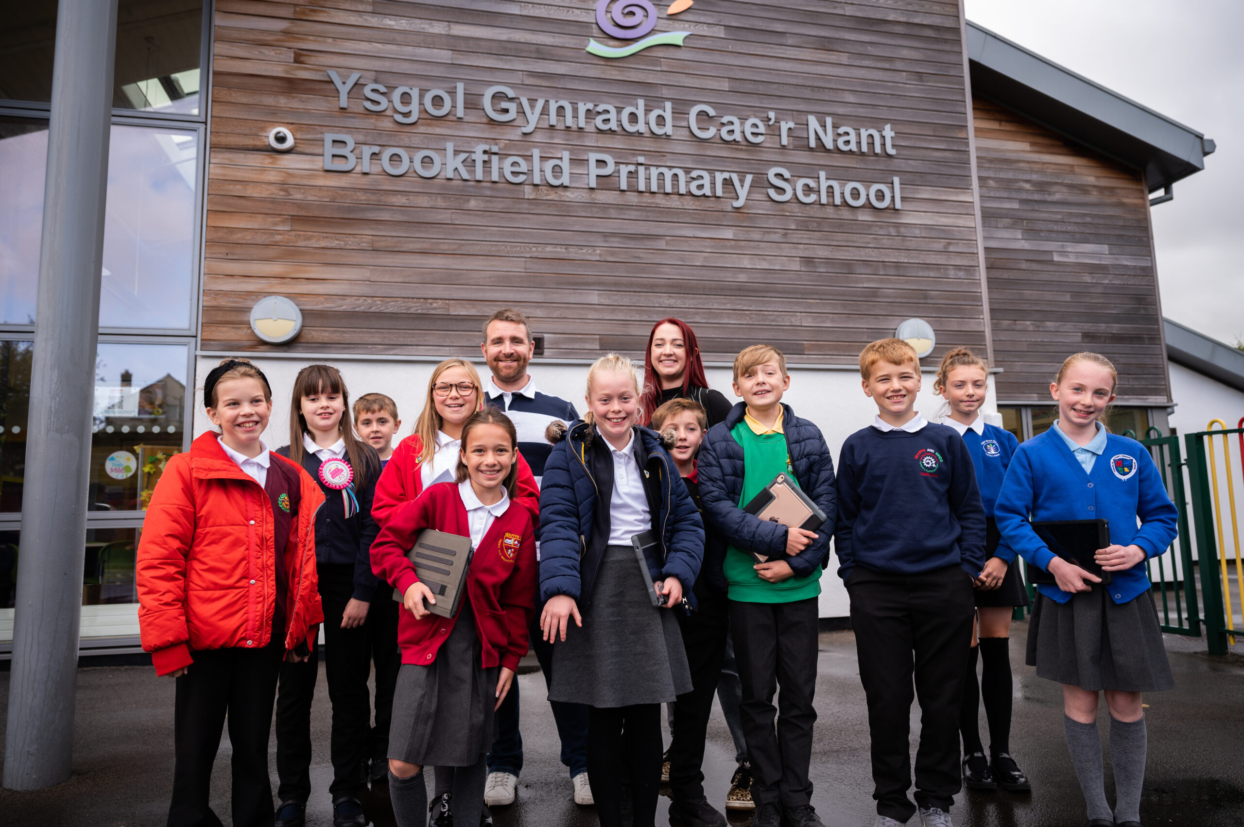 A photograph of two DCW staff members stood outside of Brookfield Primary School with ten primary school aged Digital Heroes.