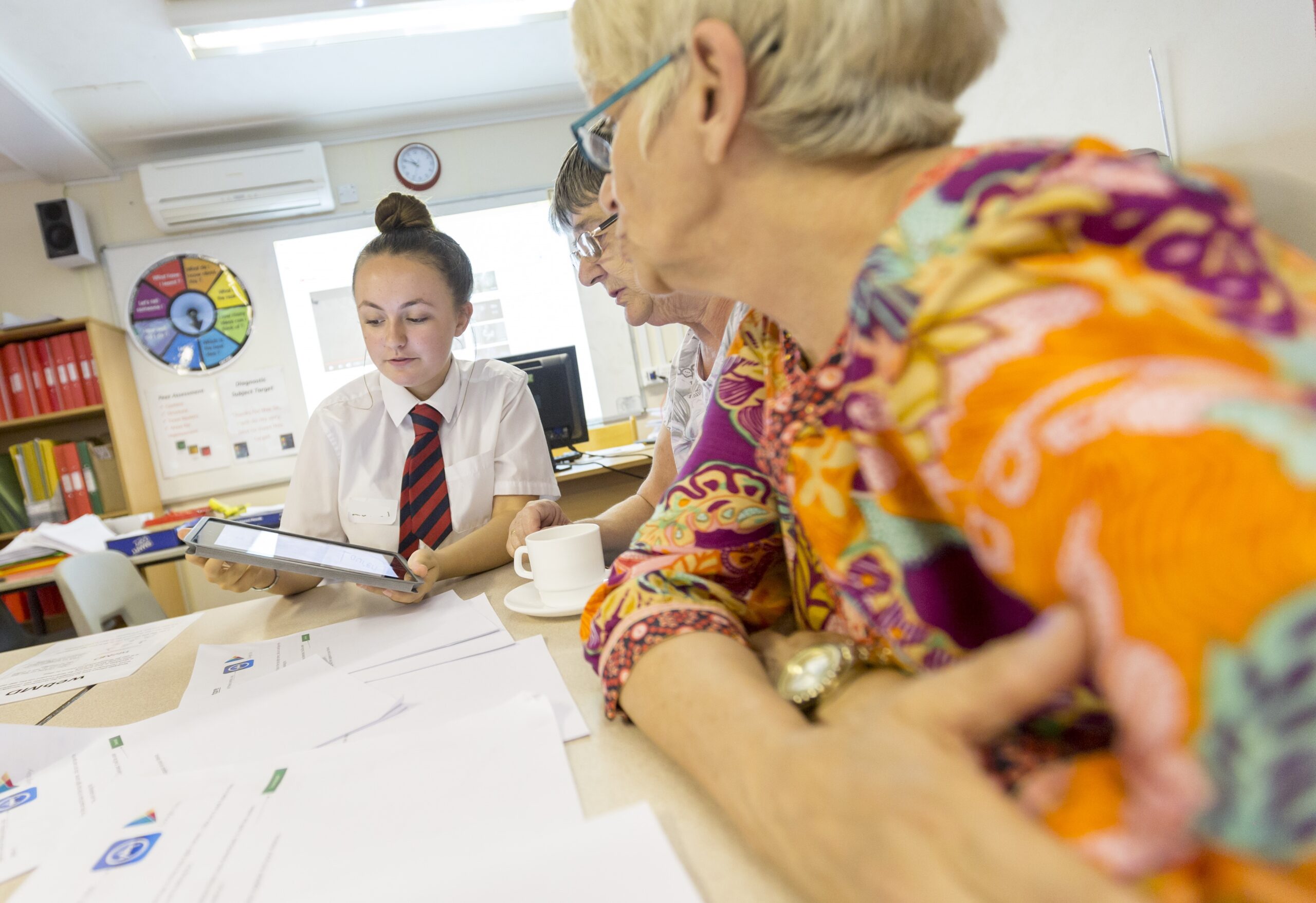 A photograph of a female Digital Hero showing two older women something on a tablet device.