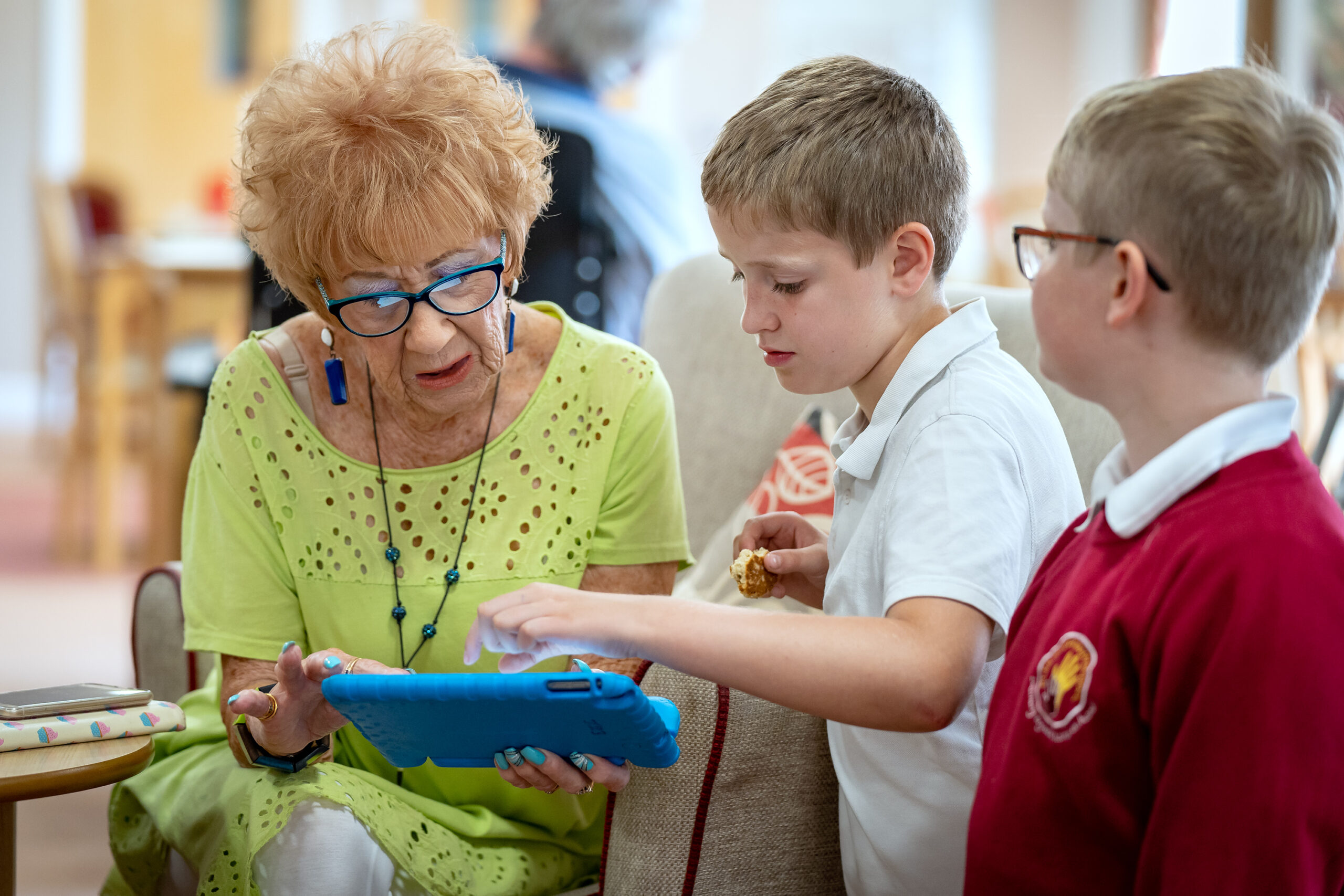 A photograph of two young male Digital Heroes showing an older woman something on a tablet device.