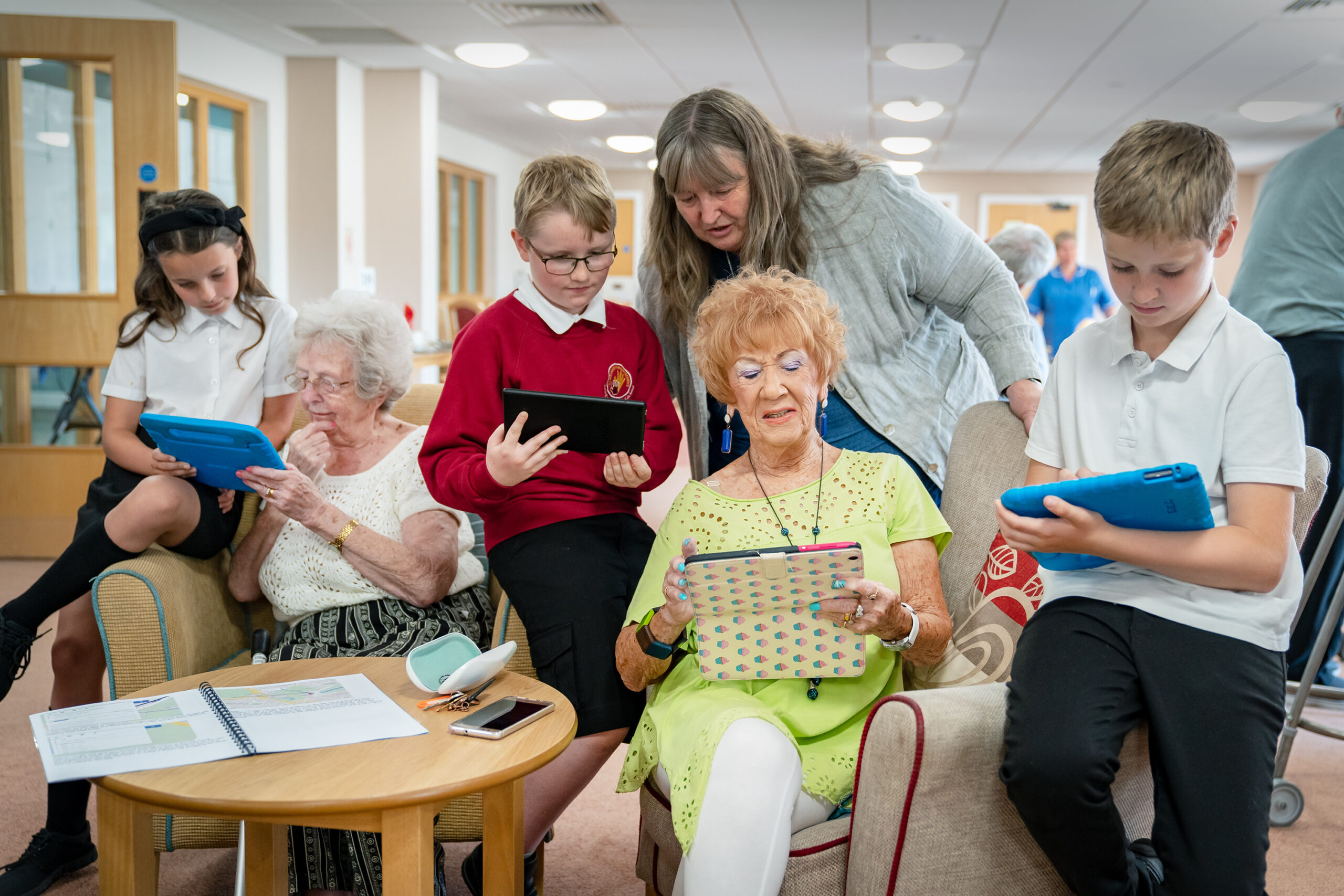A photograph of three young Digital Heroes in a care home supporting older people to use tablet devices.