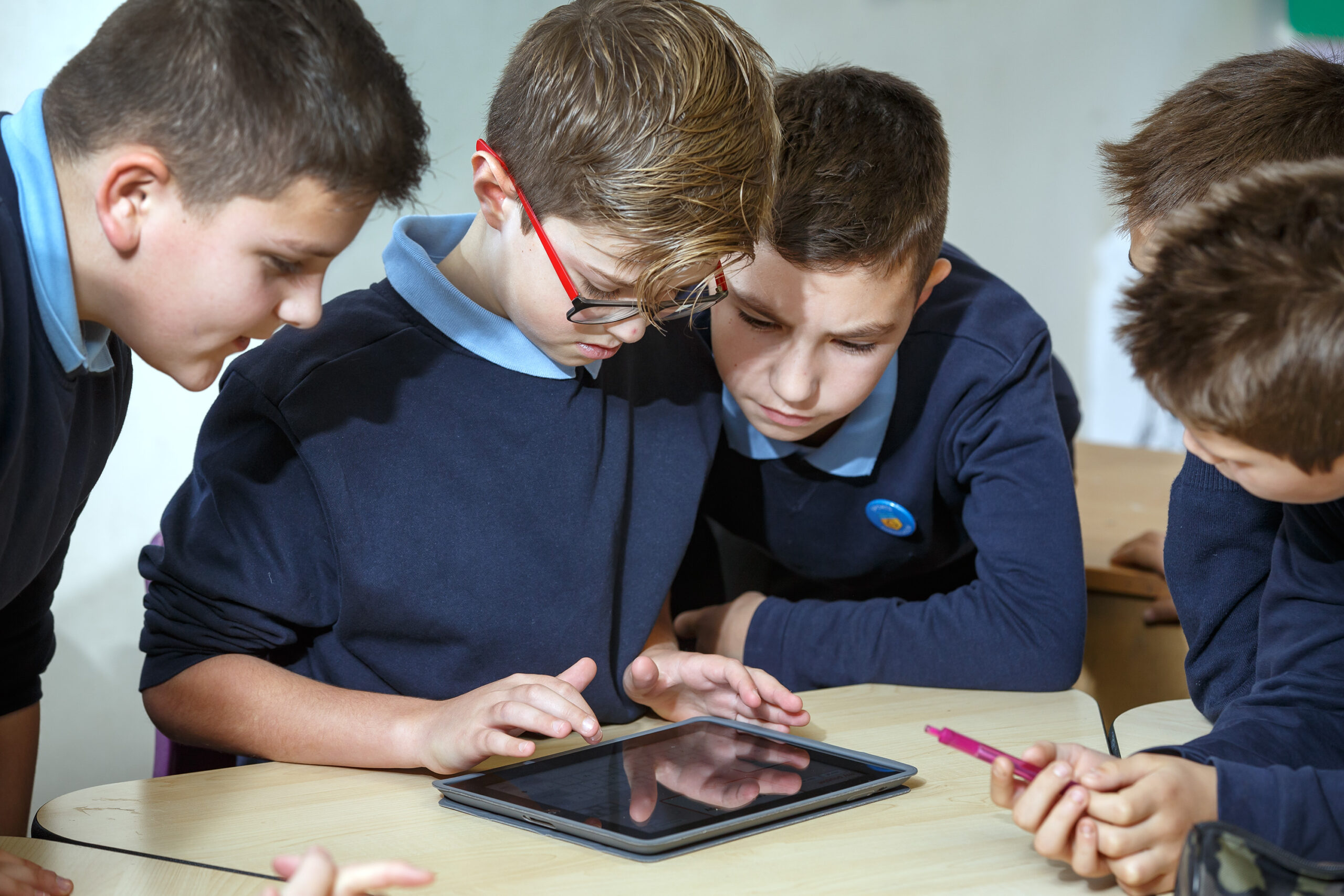 A photograph of five young male school pupils interacting with a tablet device on a desk.