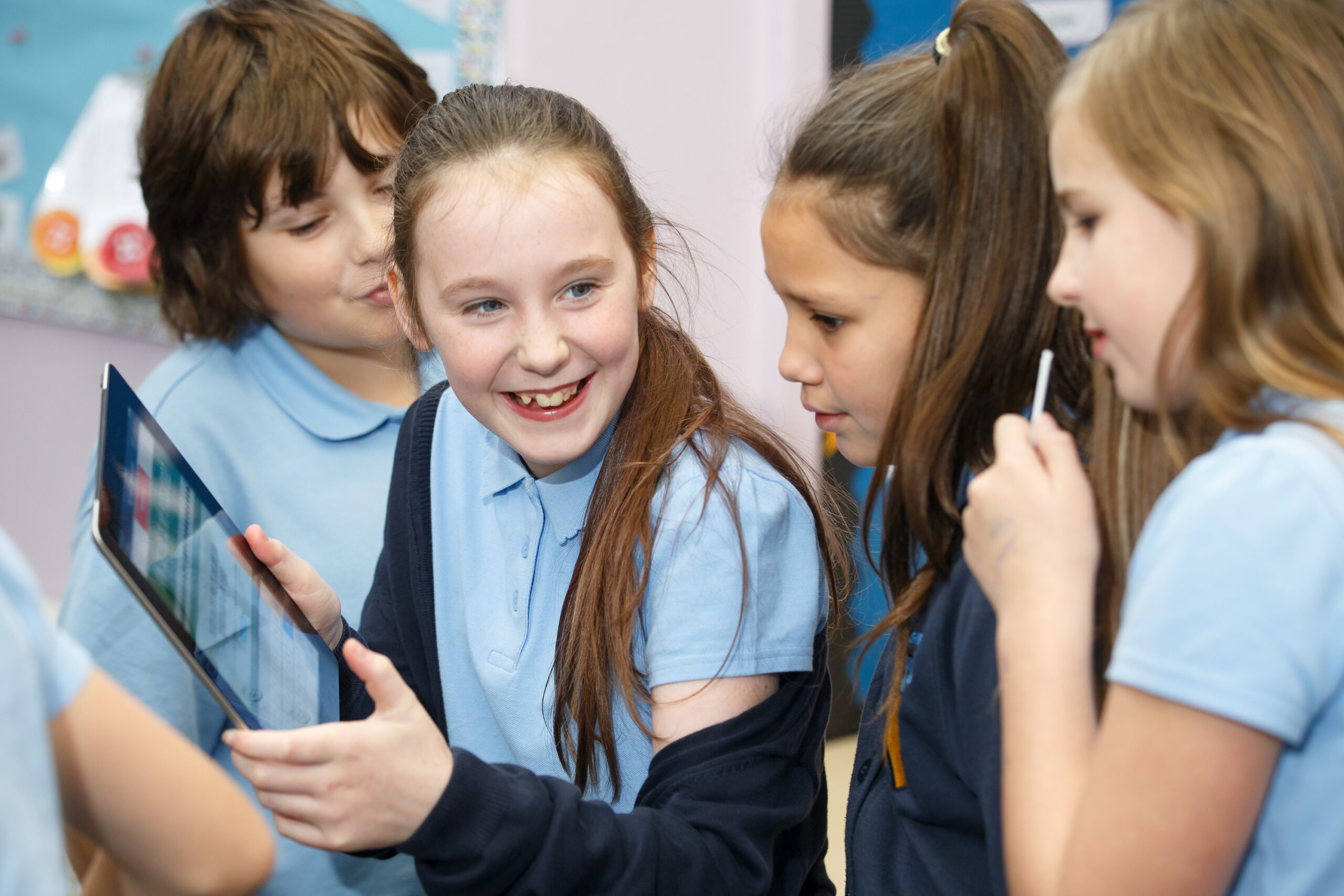 A photograph of four primary school children smiling while interacting with a tablet device