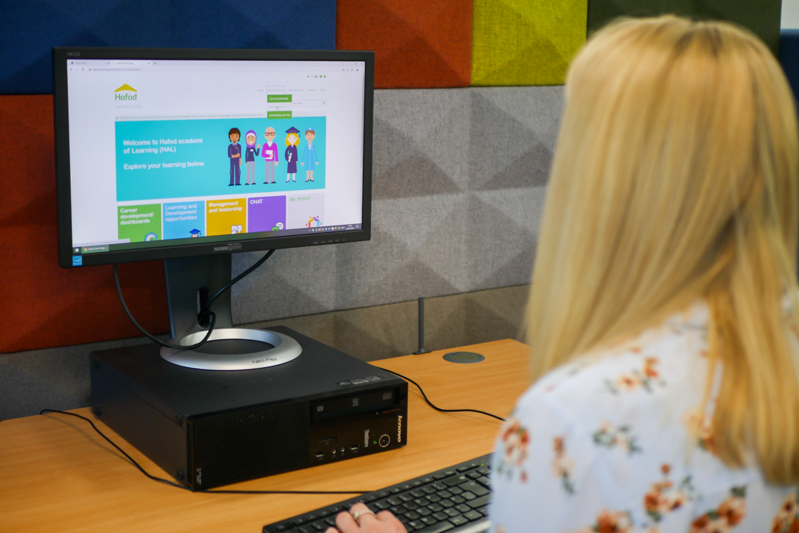 A woman sits at a desk browsing the Hafod website on a desktop computer.