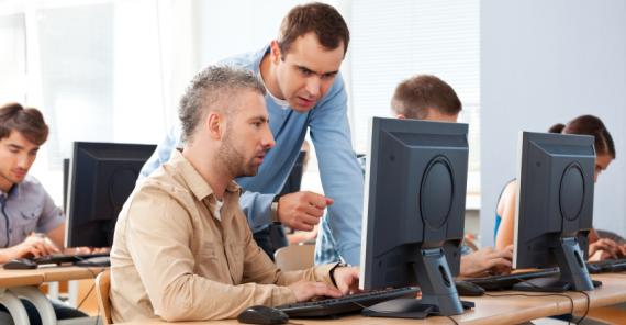 A man teaching someone how to use a computer.