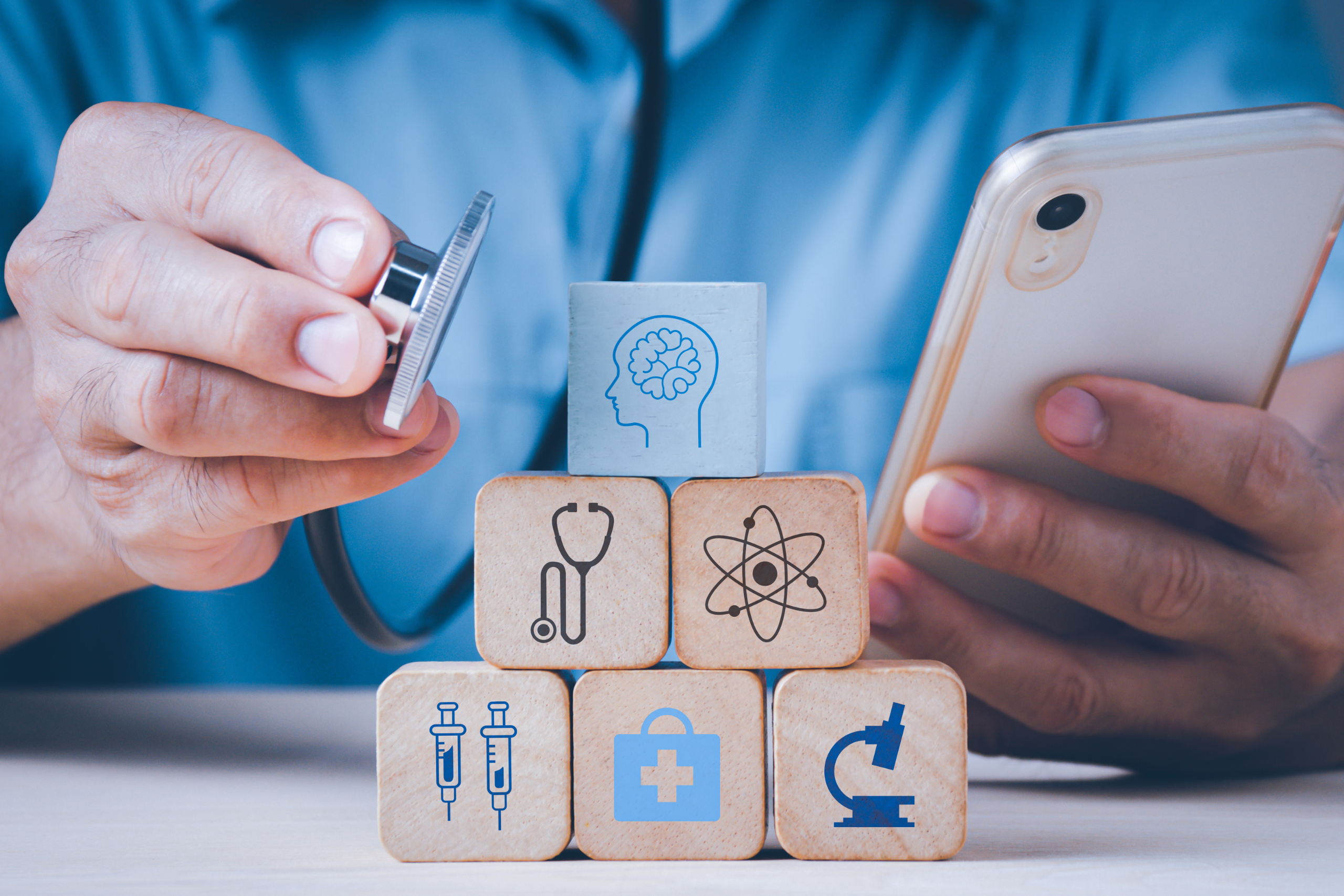 A medical professional holding a phone and a stethoscope. Infront of them are some blocks showing different medical tools.