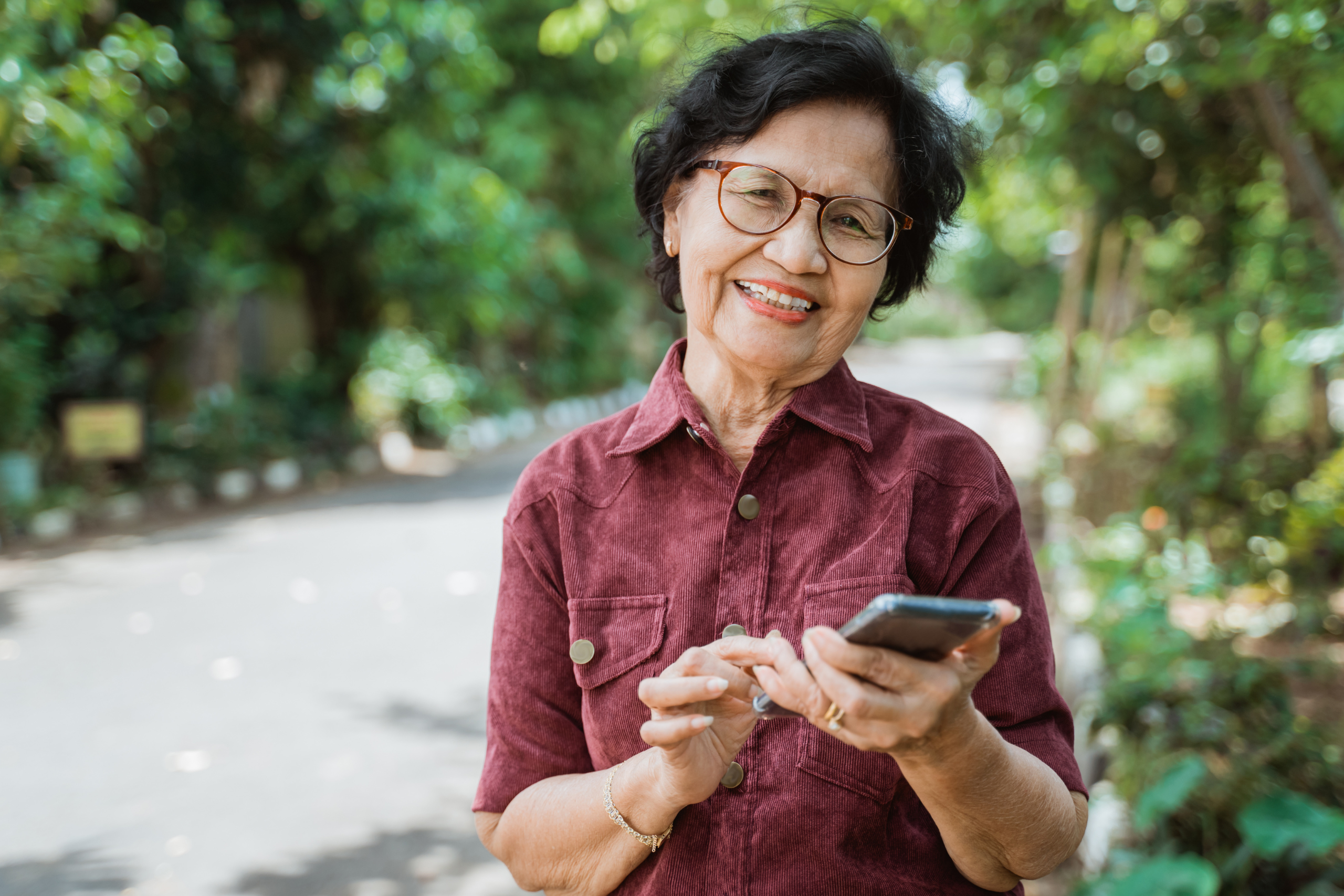 A senior woman smiles while holding a mobile phone.