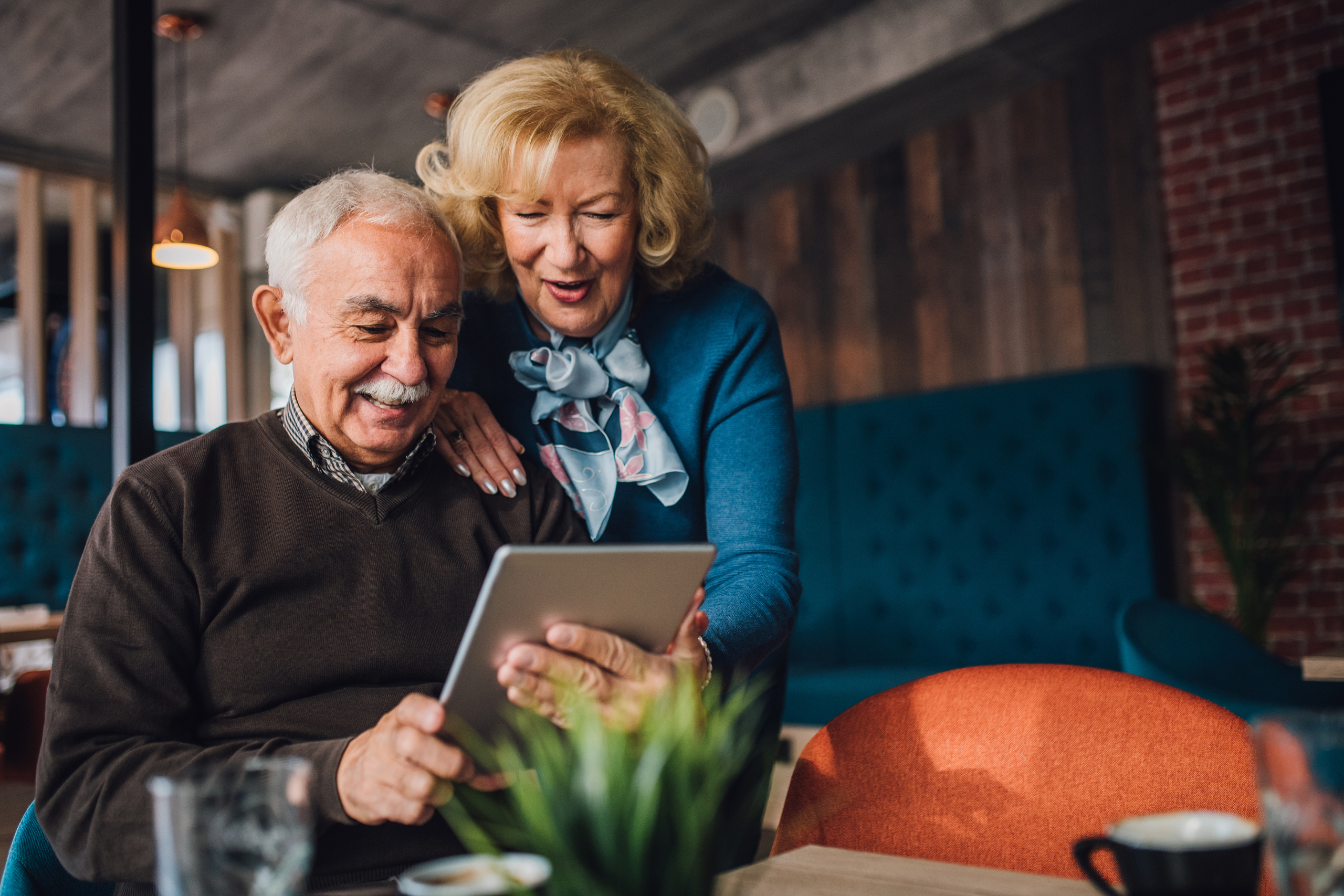 A senior man and woman smile while looking at a tablet device.