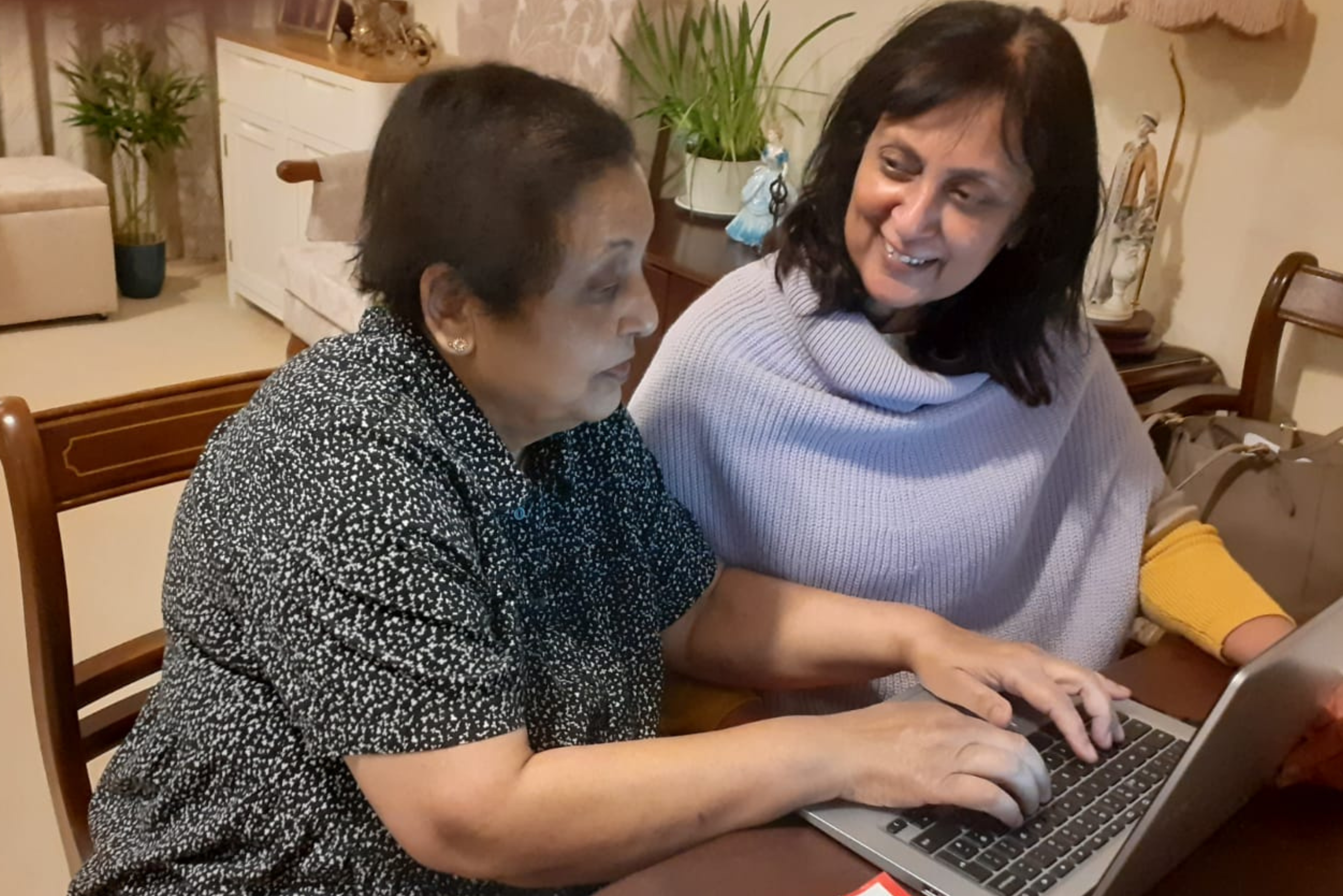 An older woman receiving help to use a laptop