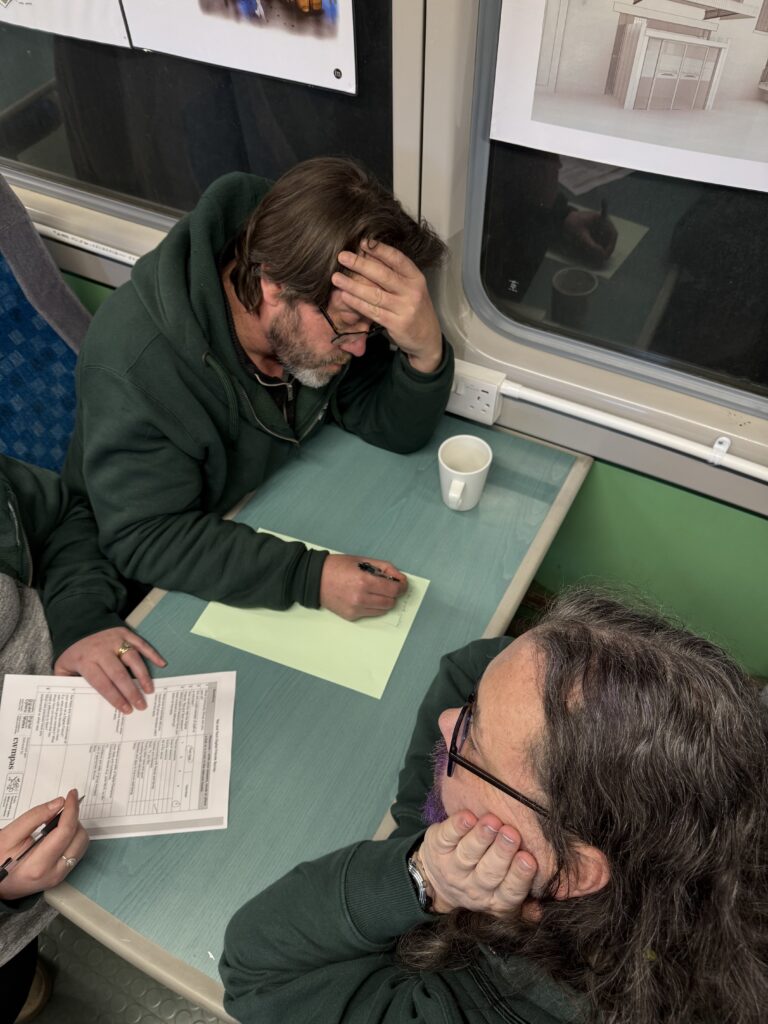 two men in green sweaters working across a table from each other