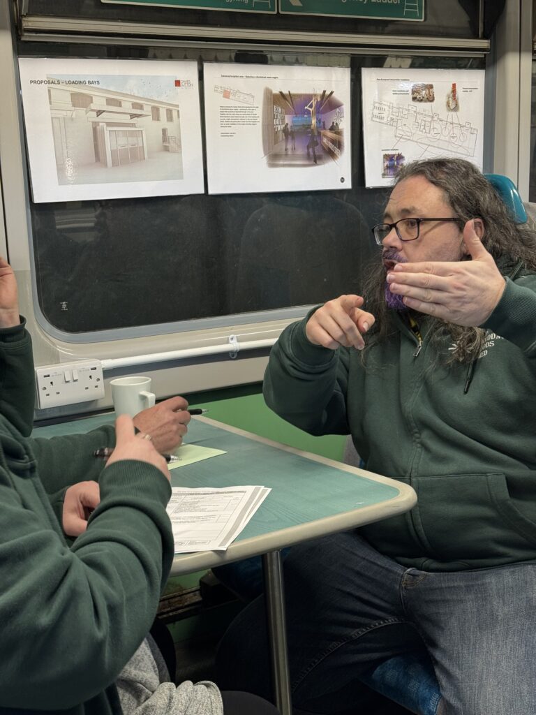 two men in green sweaters talking while sitting at a table